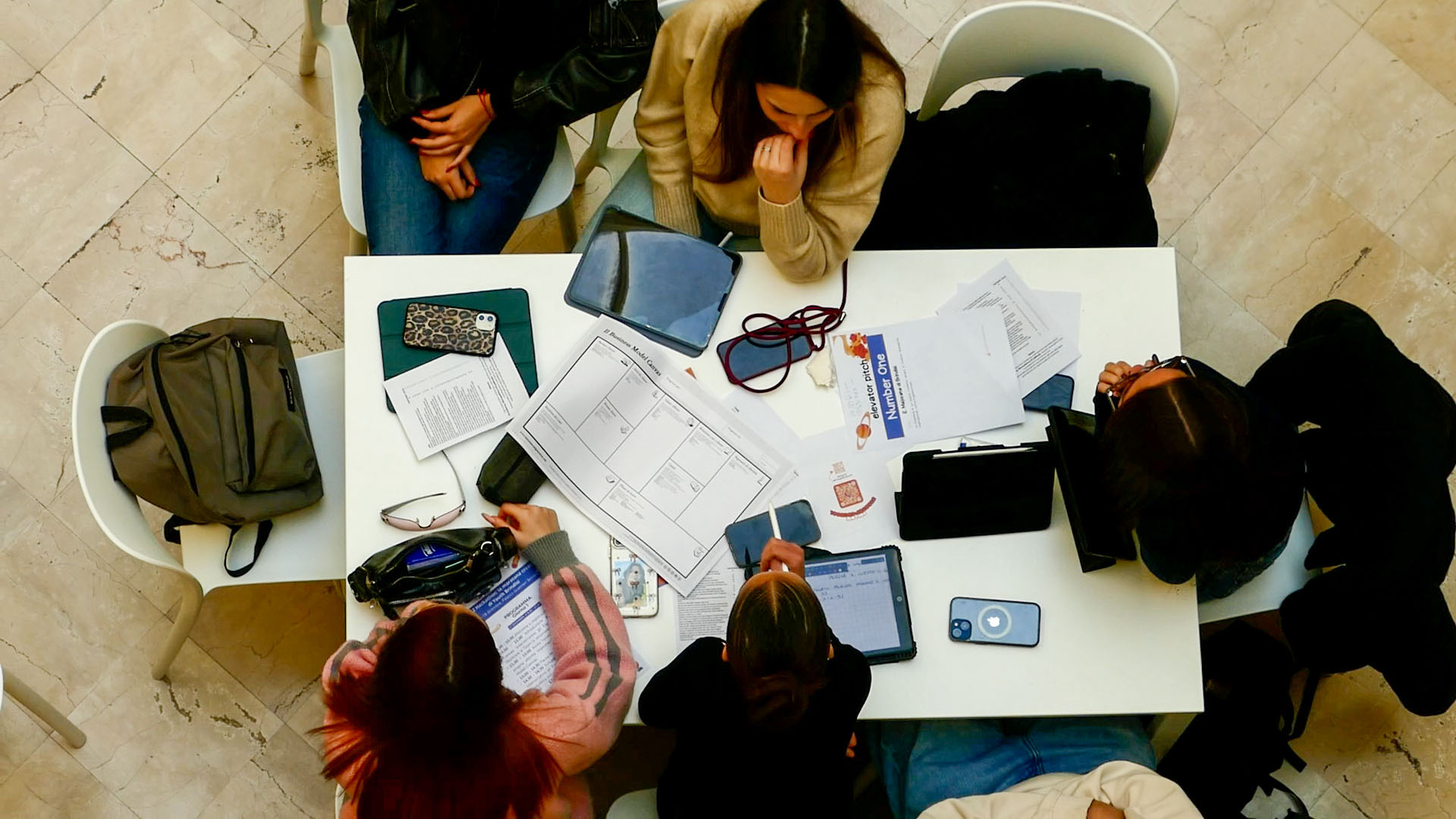 Un tavolo di lavoro visto dall’alto, con appunti, tablet e un business model canvas
