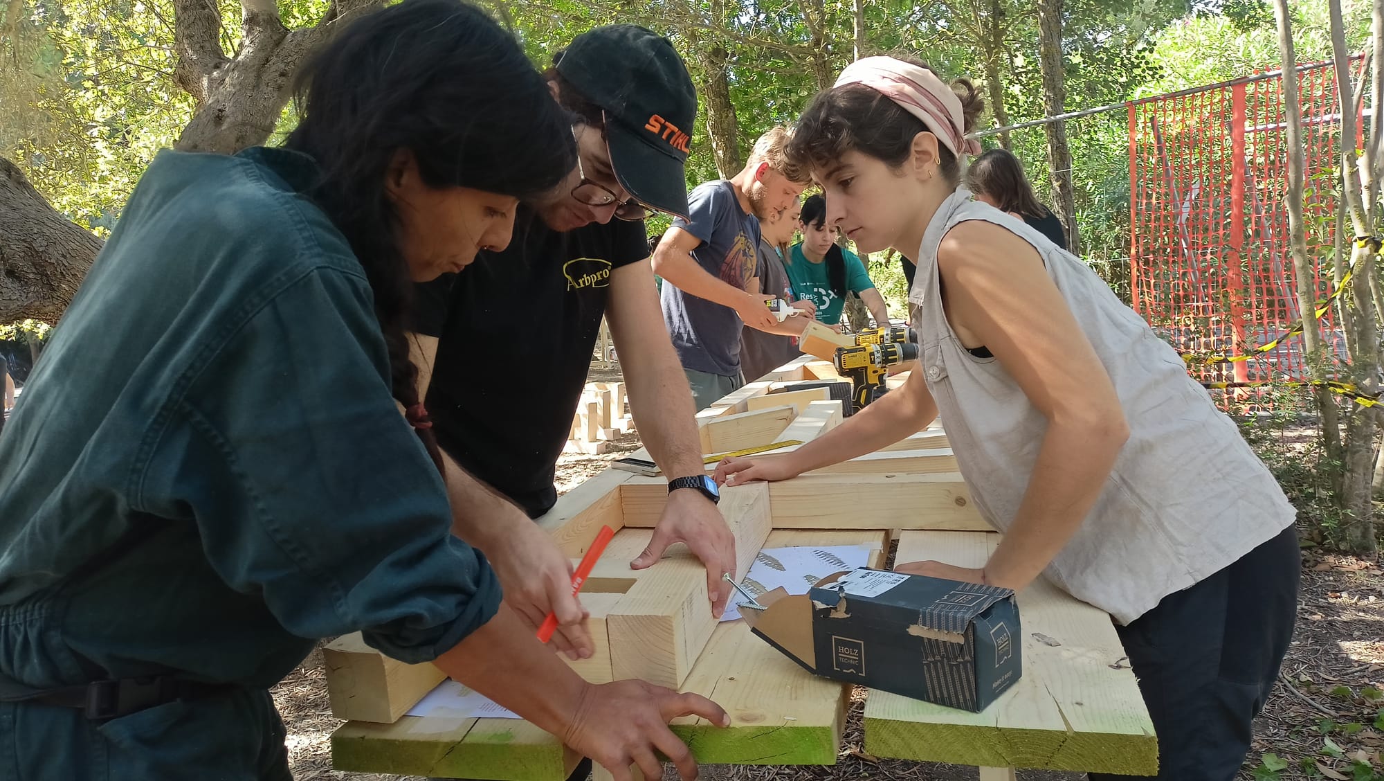 Tre persone chine su un banco di travetti: una segna un incastro con la matita, un’altra tiene fermo il pezzo.