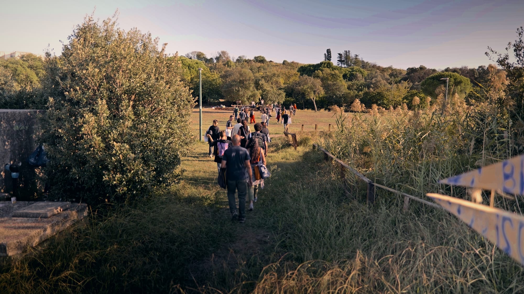 Il gruppo cammina lungo un sentiero d’erba verso il grande prato, nella luce dorata.